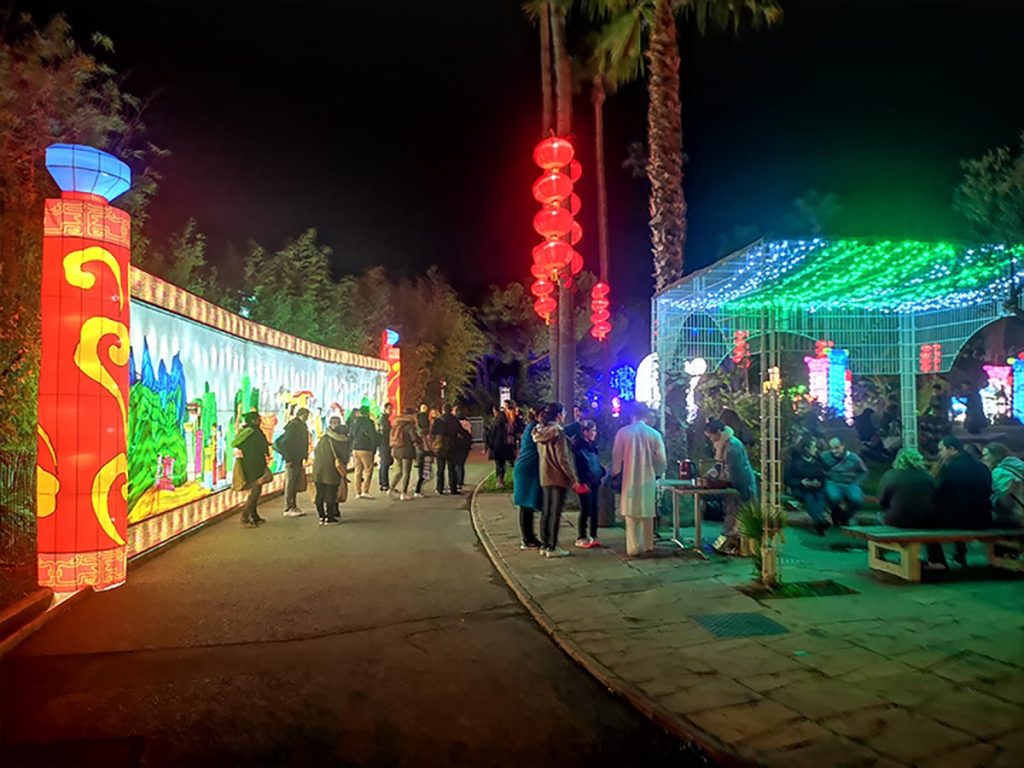 Visitors walking a lit lantern walkway at a botanical garden lantern festival