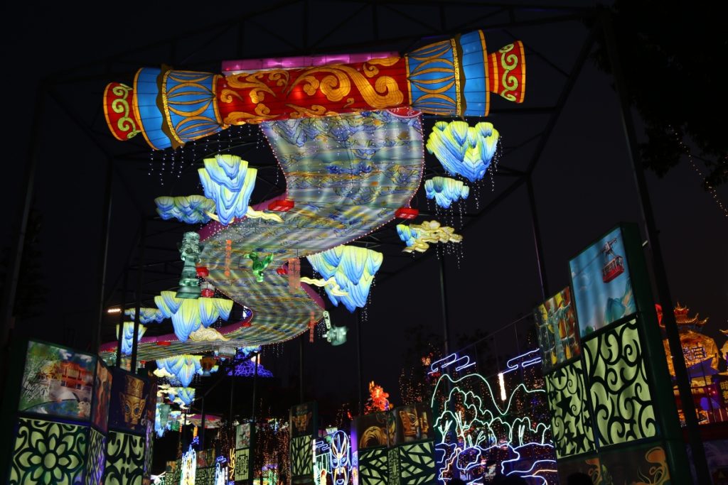 Colorful Zigong lantern festival corridor featuring hanging scroll-shaped lanterns, blue cloud lanterns, and traditional painted frame displays showcasing diverse Chinese lantern art styles