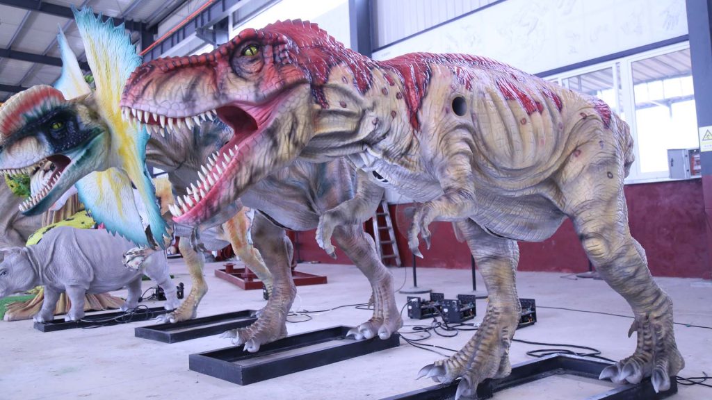 Two life size animatronic dinosaurs — Spinosaurus and Dilophosaurus — standing in factory showroom for client inspection and delivery preparation.