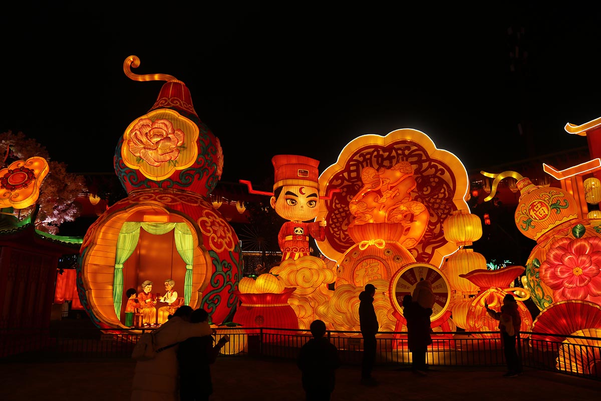 Blessing lantern — illuminated Fu character and gourd with peony motifs and a family scene inside, lit red and gold at night