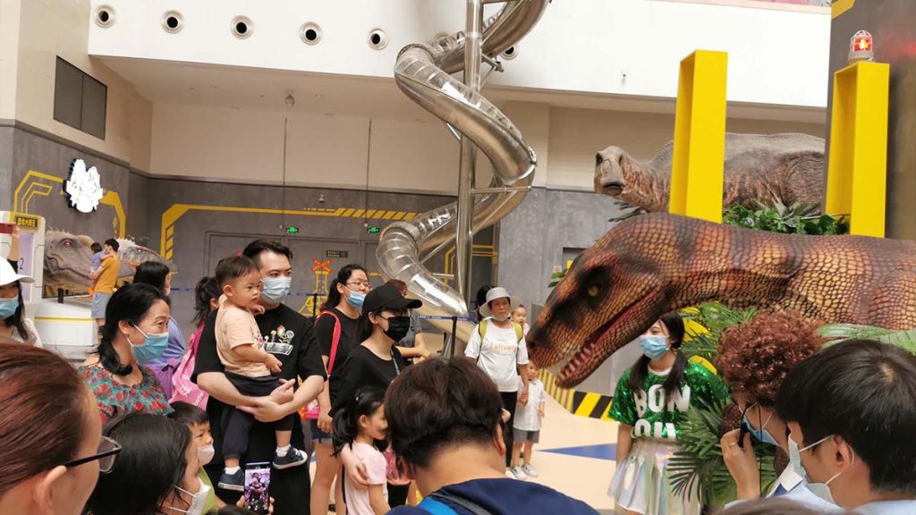 Children and families watching a life-size animatronic dinosaur show at a theme park attraction