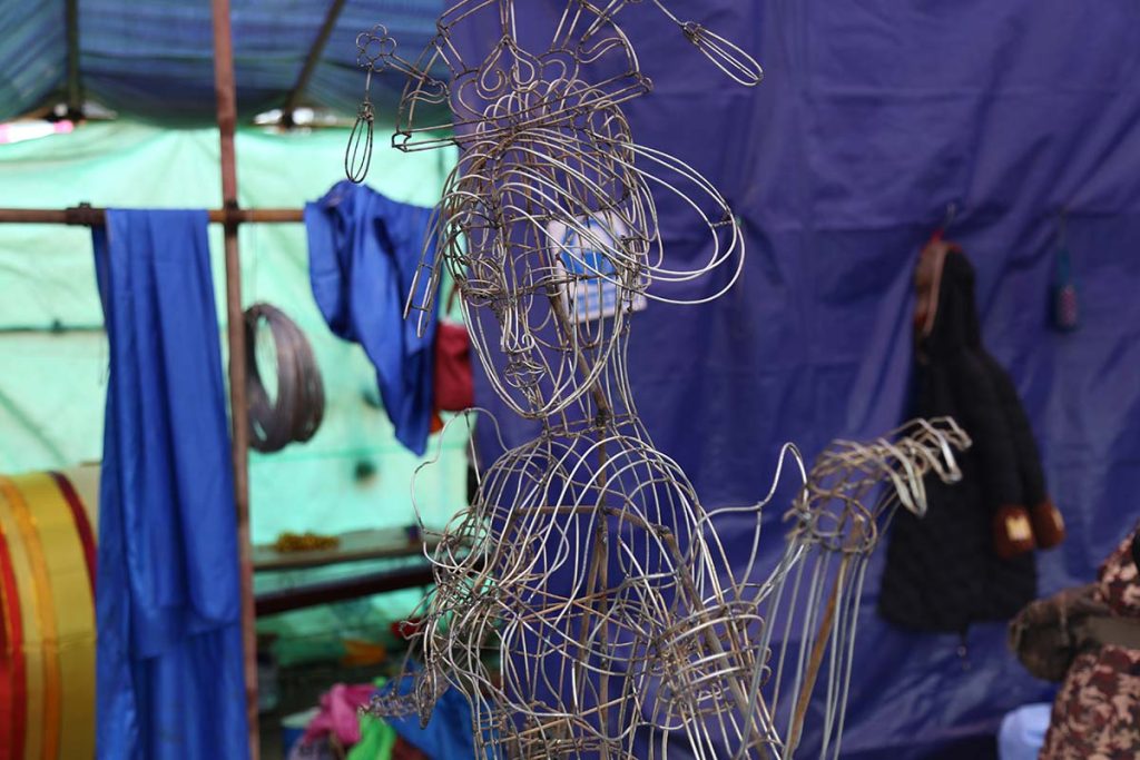 Bare wire frame of a Zigong lantern figure under construction showing the interplay of (contour-following wires defining the face and flowing elements) and (cross-sectional rings defining volume) before silk is applied