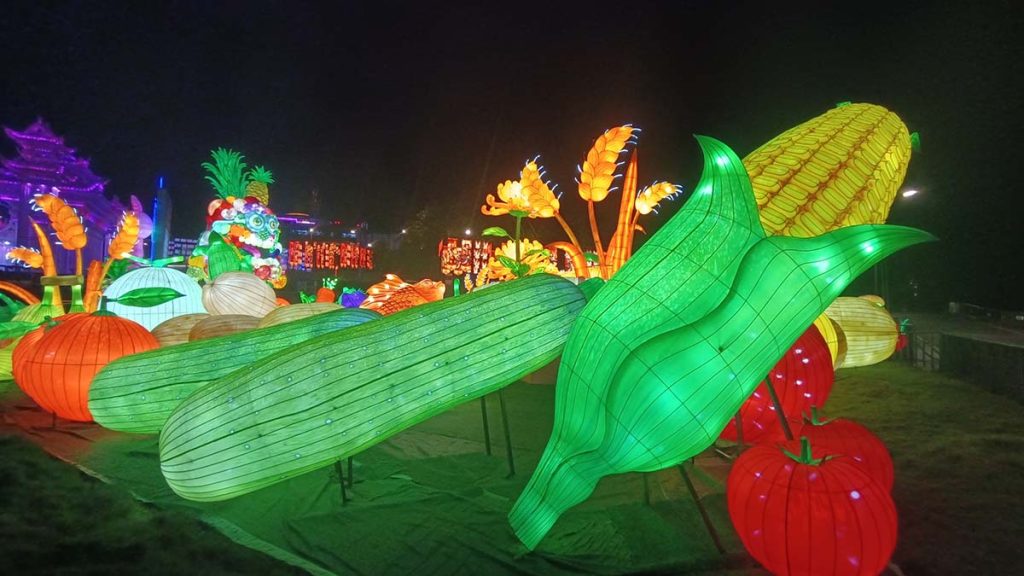 Giant illuminated harvest vegetable lanterns including corn, tomato, cucumber and pumpkin on display at an outdoor food festival
