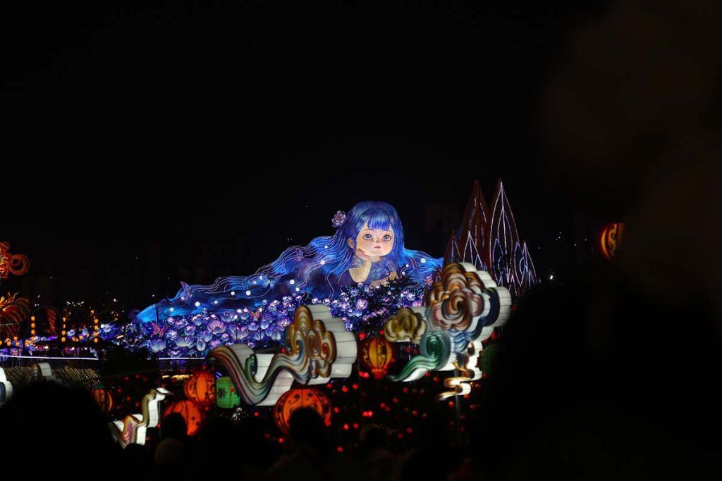 Giant illuminated girl figure surrounded by glowing flowers and lotus lanterns at a festival display, demonstrating the scale and visual impact of Chinese lantern centrepieces