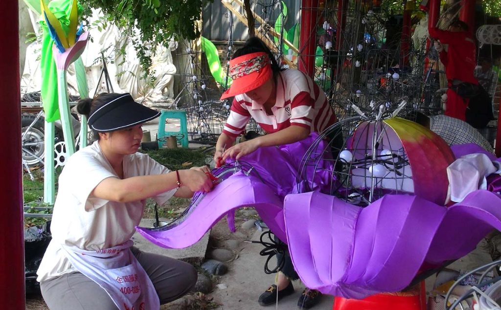 Two skilled artisans hand-stitching colorful silk fabric onto a steel lantern frame — traditional Zigong craftsmanship