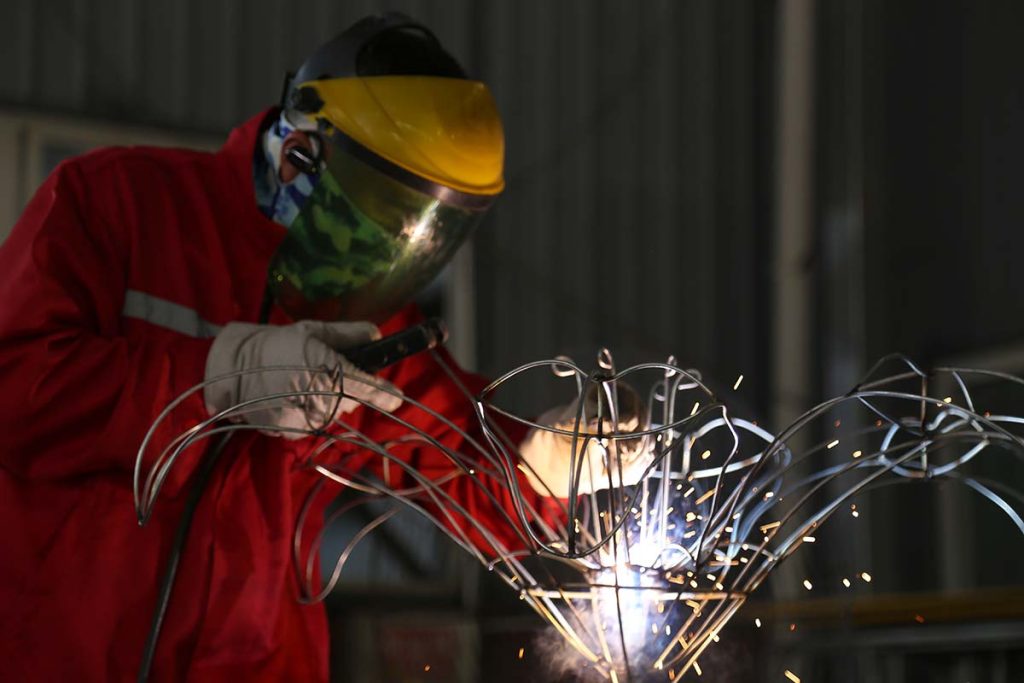 Worker in protective gear welding galvanized steel frame for festival lantern — precision metalwork in factory