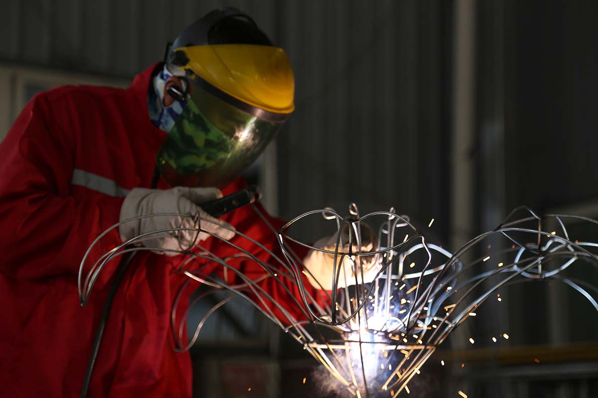 Welding the frame of a large lantern on the workshop floor