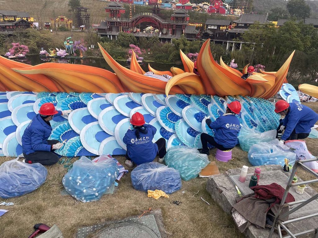 Workers installing recycled plastic water bottles into giant Chinese dragon lantern as part of sustainability-focused craftsmanship