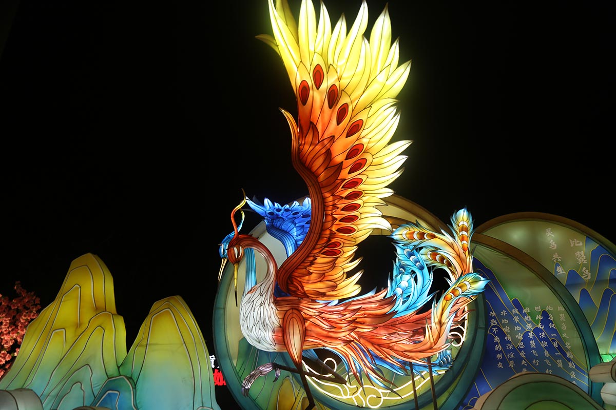 Mandarin duck lantern — a pair of illuminated love birds flying together in front of a lit moon and cloud backdrop