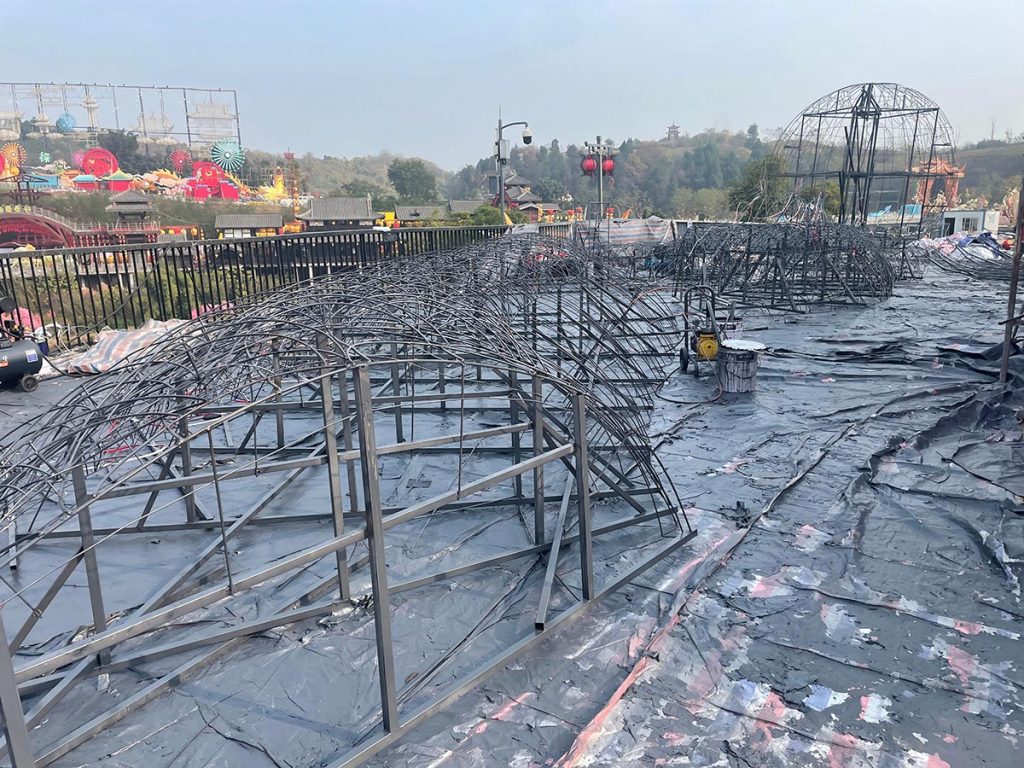 On-site production yard of a large-scale lantern festival with multiple arched steel skeleton frames laid out for silk application and final assembly.