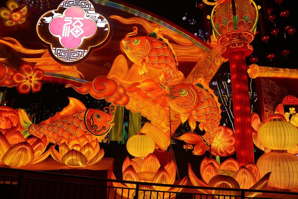 Large illuminated koi fish lantern with the 福 (fortune) character surrounded by lotus pods and traditional Chinese lanterns, representing the classic 年年有鱼 (nian nian you yu, "abundance year after year") festival symbol | Nian Nian You Yu Koi Fish Lantern