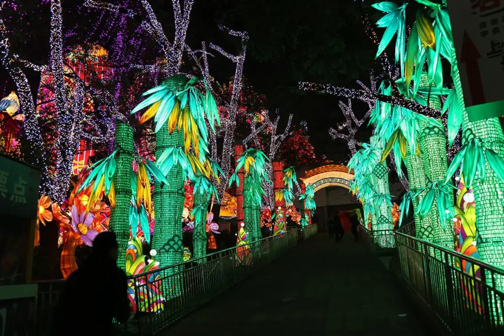 Immersive walk-through bamboo forest corridor lantern display with illuminated green glass-bottle bamboo stalks and cascading silk leaves lining a festival pathway at night