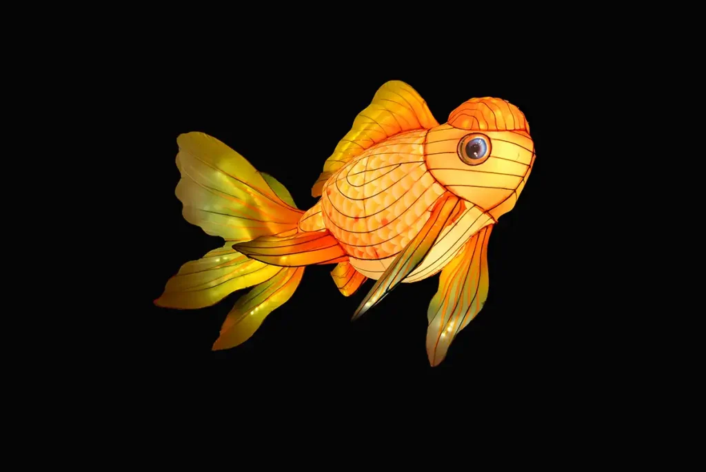 Handcrafted illuminated goldfish lantern in classic Chinese style with flowing fins, peacock-eye scales, and warm orange LED glow against black background