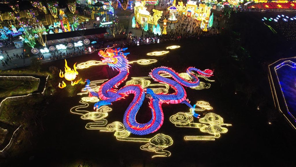Aerial view of giant programmable RGB Chinese dragon lantern displaying dynamic red and blue color zones in a festival park at night