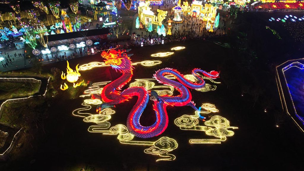 Aerial view of giant programmable RGB Chinese dragon lantern glowing in vivid red and pink color in a festival park at night