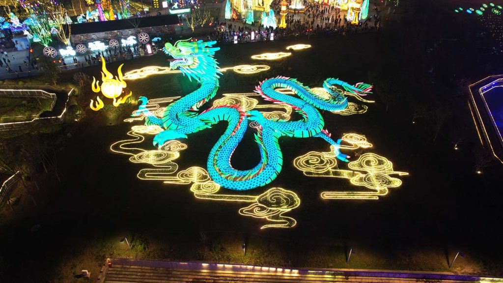 Aerial view of giant programmable RGB Chinese dragon lantern glowing in green and cyan color in a festival park at night