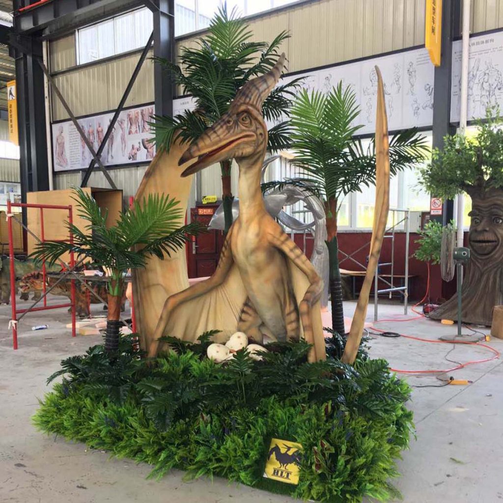 Life-size animatronic Pterosaur (flying reptile) with long neck, beak, and folded wings, displayed in a themed palm-tree and fern exhibit. Prehistoric flying reptile suitable for theme park and museum dinosaur exhibits.