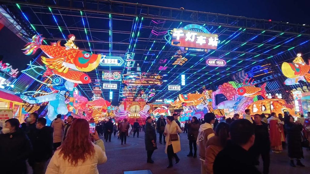Illuminated walk-through lantern tunnel corridor display at night festival with glowing ceiling and hanging lanterns for immersive experience