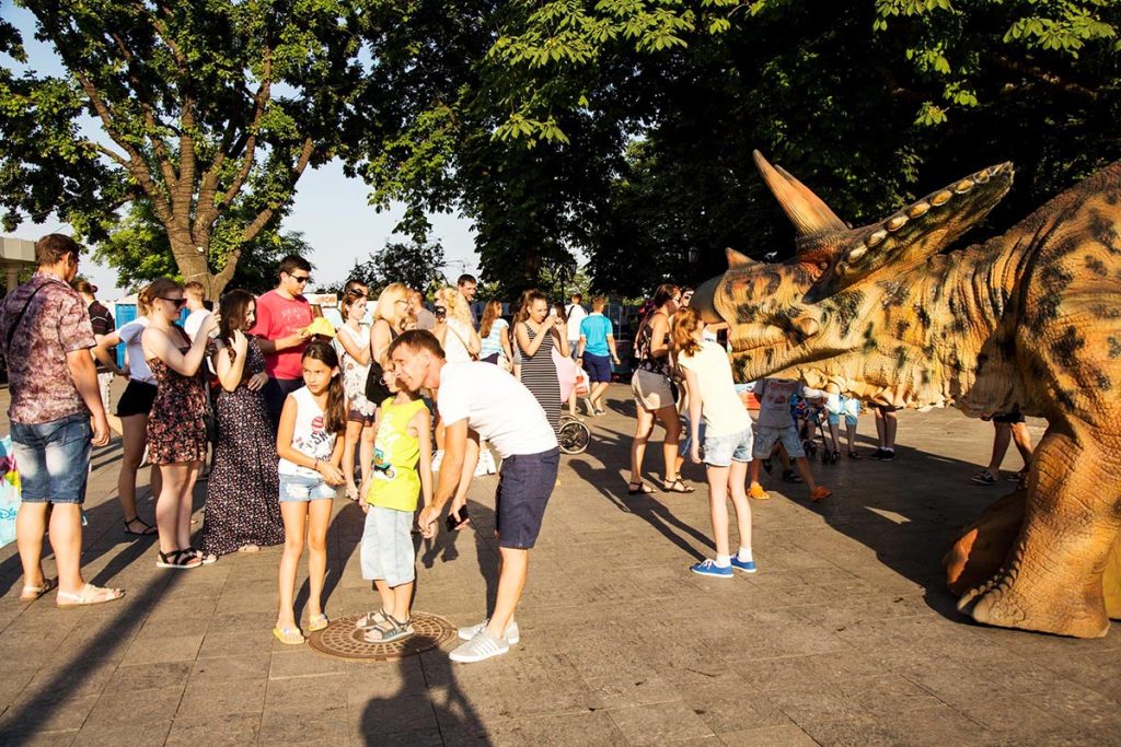Walking animatronic dinosaur street performance attracting a crowd at an outdoor festival event