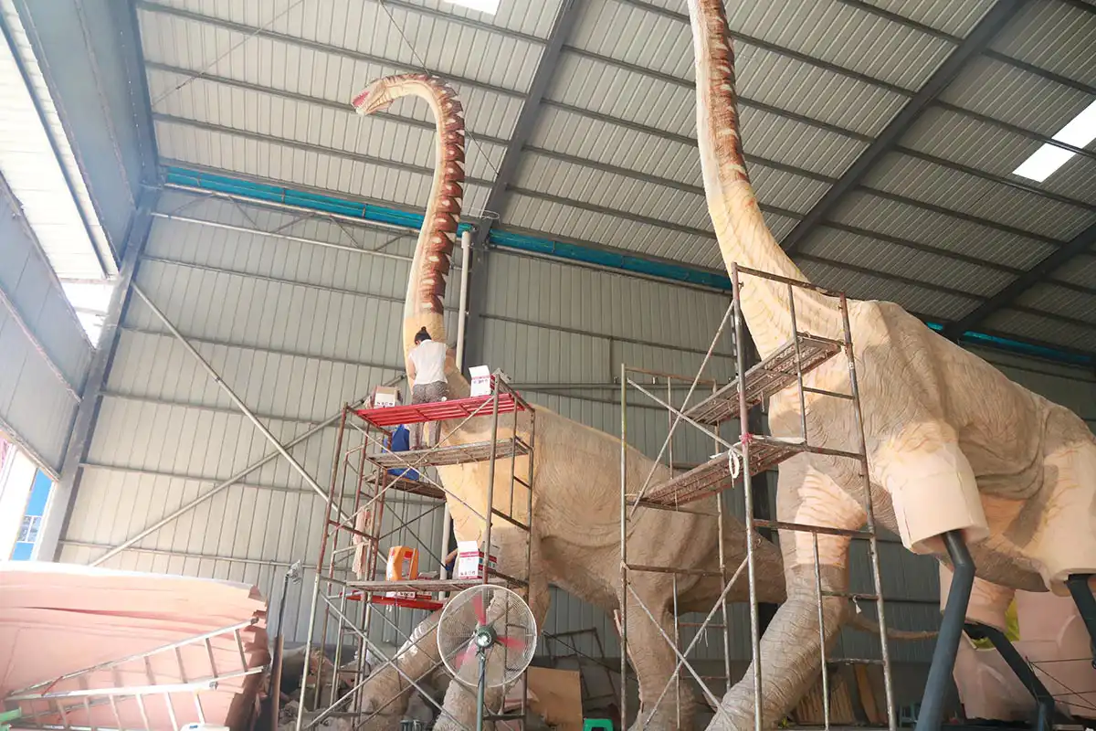 Factory workers painting silicone skin and texture details on a giant animatronic brachiosaurus for a shopping mall display