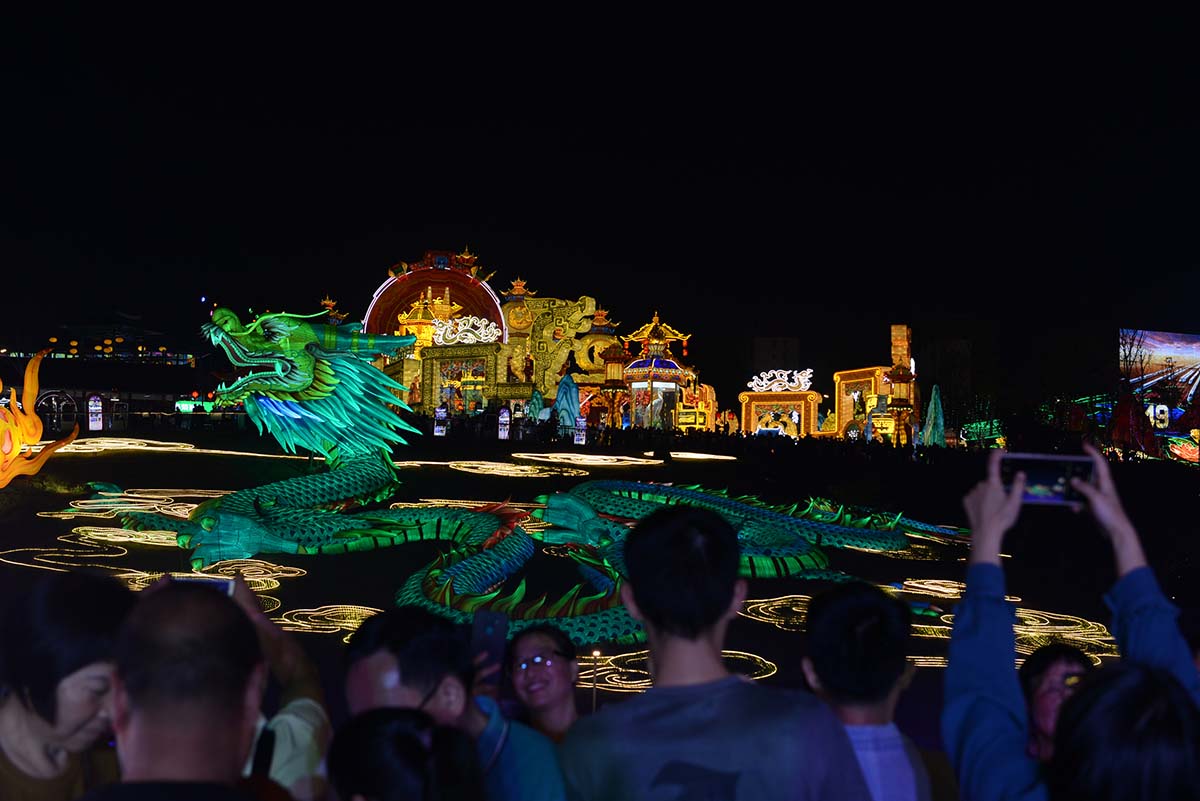 Green coiled dragon lantern sculpture with a palace gate backdrop and visitors taking photos