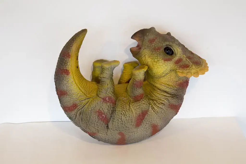 Cuddly animatronic baby triceratops puppet in curled hatchling pose with hand-painted frill