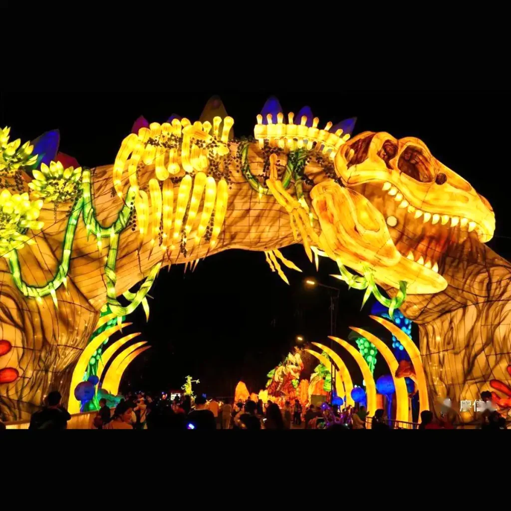 Full-size dinosaur fossil archway lantern at night with visitors walking under the rib-cage gateway