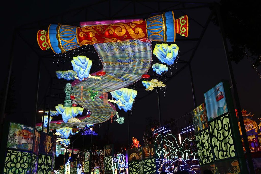 Giant Chinese scroll lantern display with illuminated landscape painting hanging above a festival courtyard