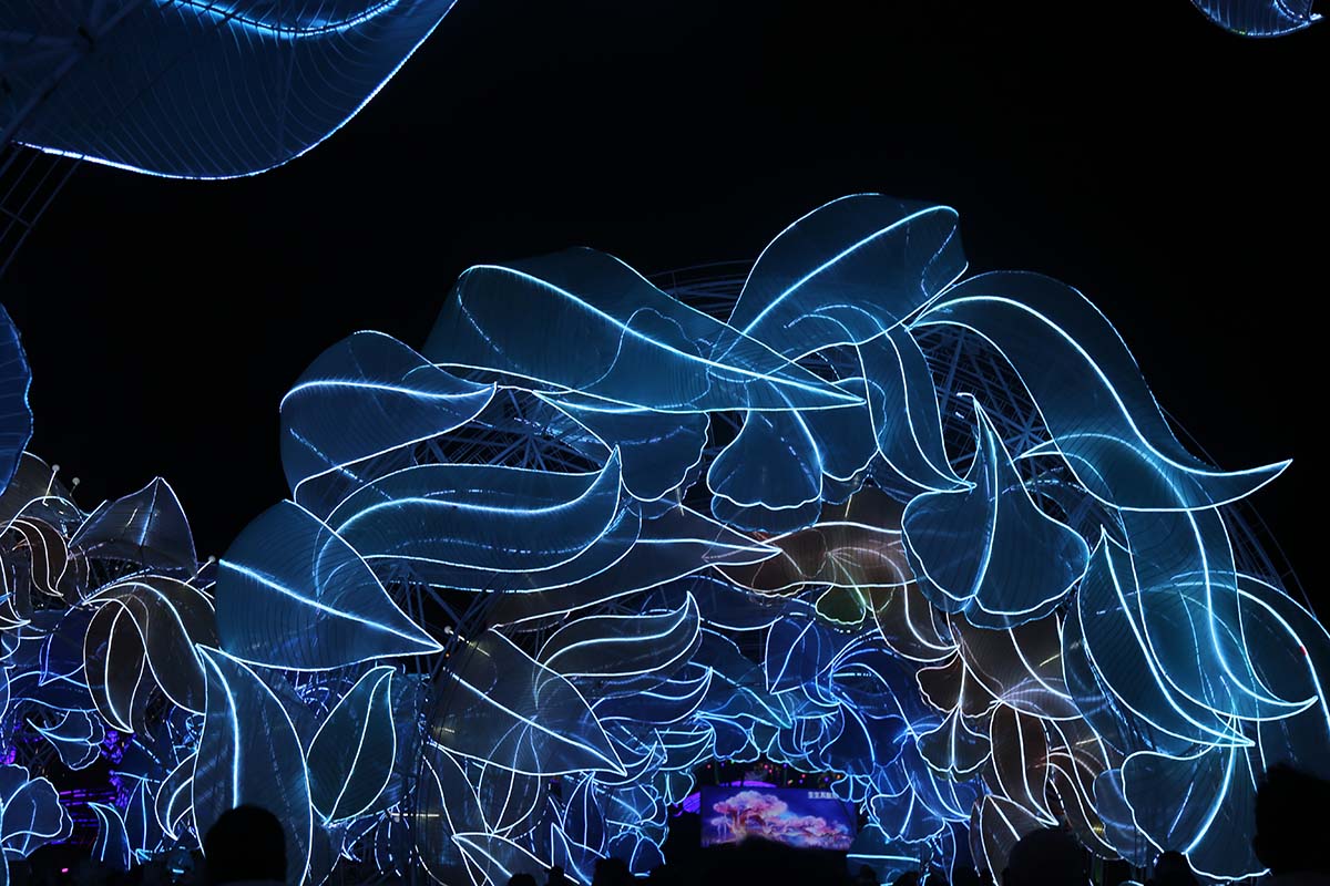 Festival visitors watch glowing LED-line animal sculptures in blue and violet at a FestiveLanterns lantern festival tunnel display