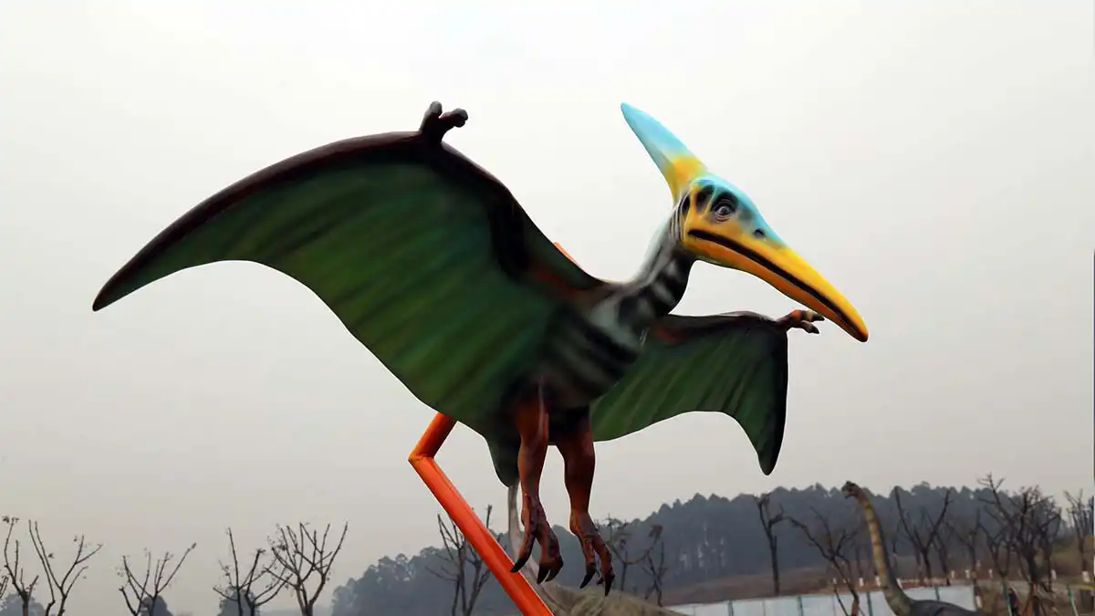 Colourful pterosaur animatronic on outdoor installation — green wings, yellow beak, blue crest — engaging visitors