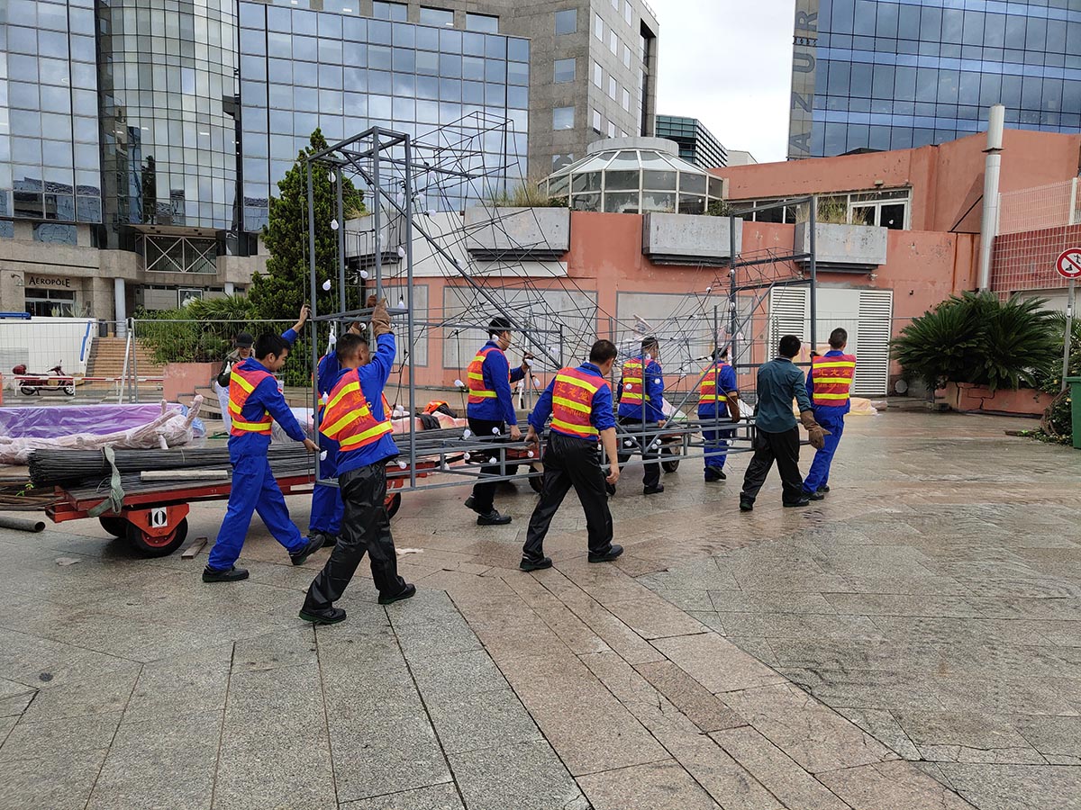 Workers carrying galvanised steel frame sections of Chinese lantern display at European venue — modular frame assembly begins immediately after delivery
