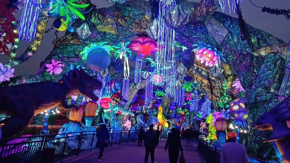 Visitors walking beneath a canopy of glowing flowers, jellyfish lanterns, and vine installations at a FestiveLanterns winter lantern festival