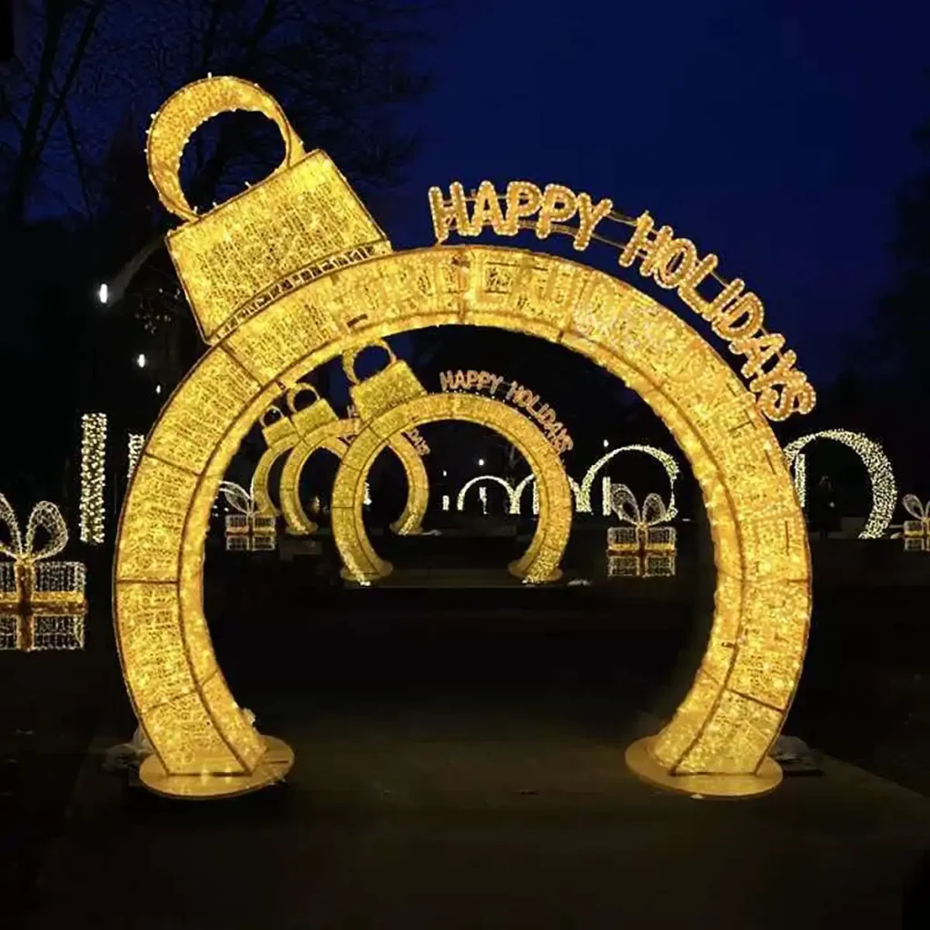 Happy Holidays ornament archway light display with illuminated letters, gift boxes and ornament balls at night