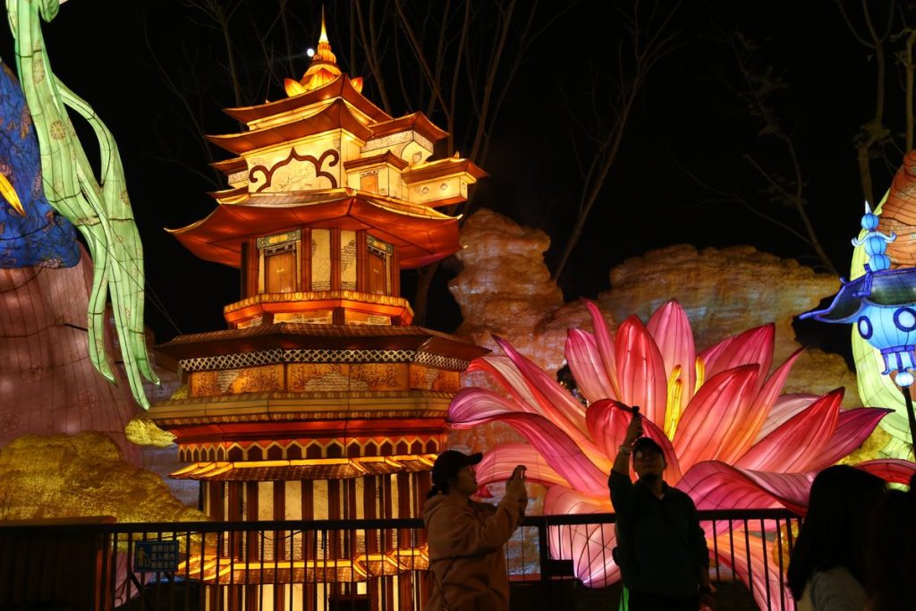 Chinese pagoda lantern glowing in golden light beside giant pink lotus lanterns at a night festival