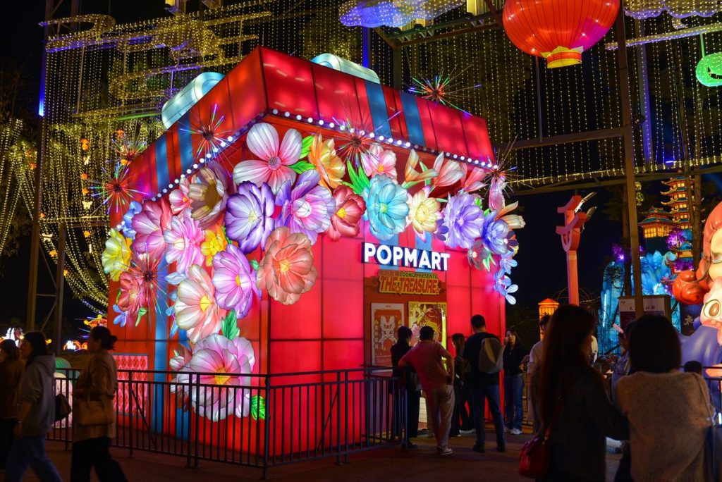 Giant gift box lantern kiosk wrapped in glowing flower lanterns serving as an illuminated retail pavilion