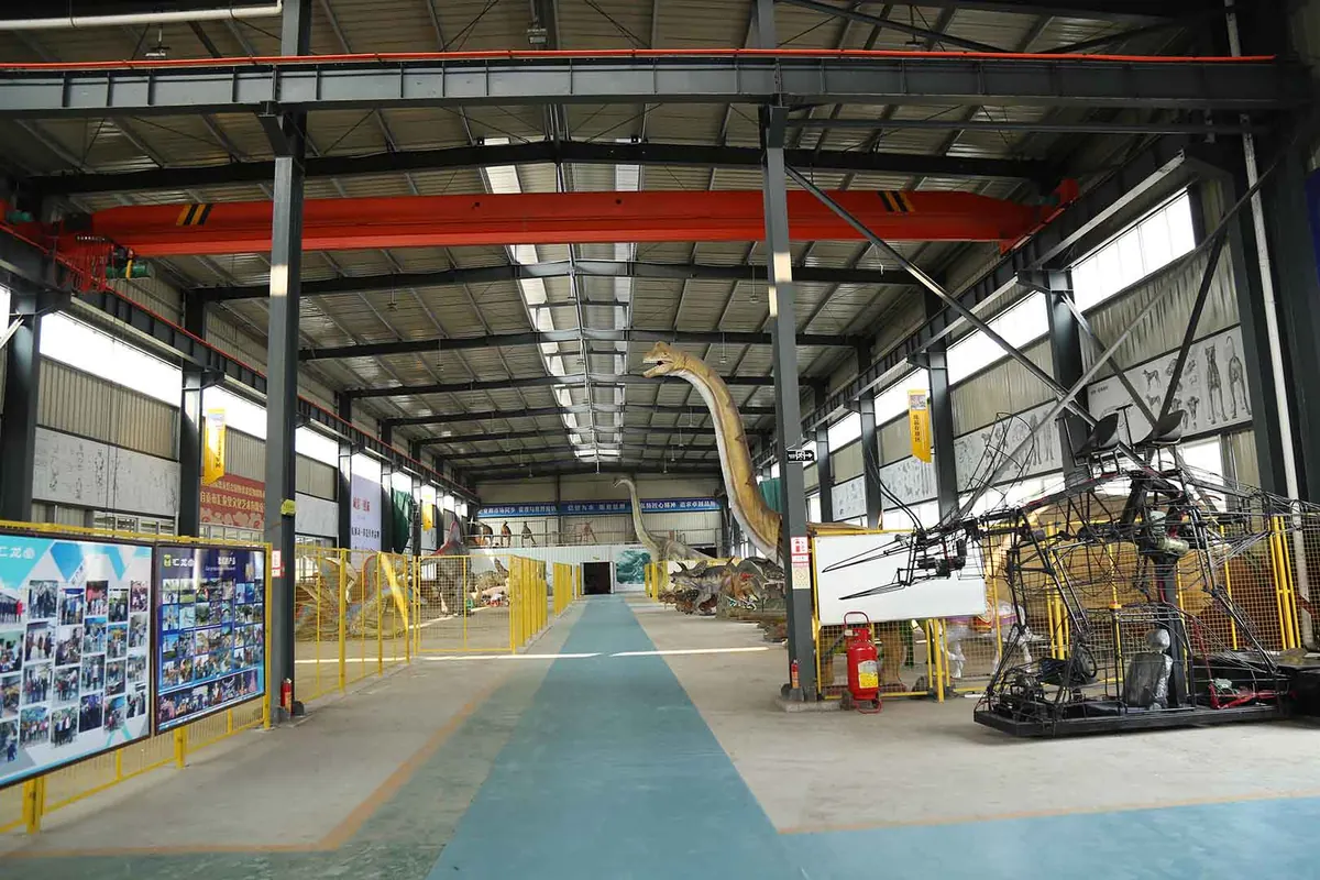 Interior of the FestiveLanterns production workshop where large dinosaur displays are assembled under the crane bay