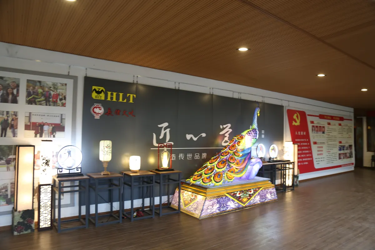 Showroom at the FestiveLanterns production base displaying finished lantern lamps and a peacock lantern beside the company brand wall