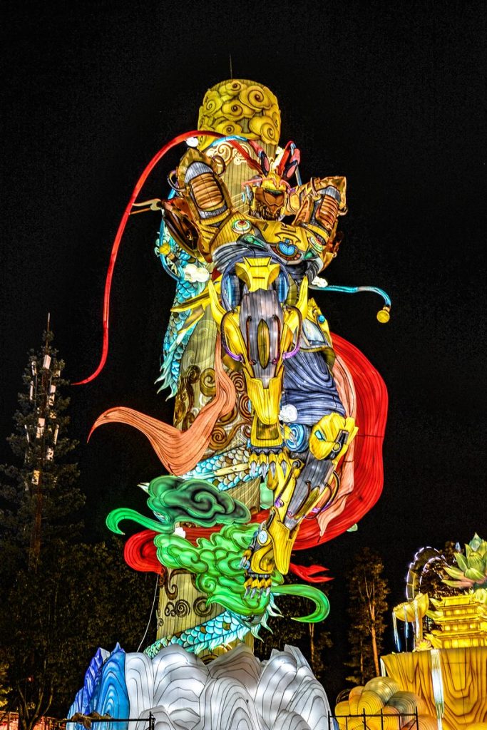 Giant Monkey King lantern sculpture in golden armour standing on a cloud base with a green dragon coiling below