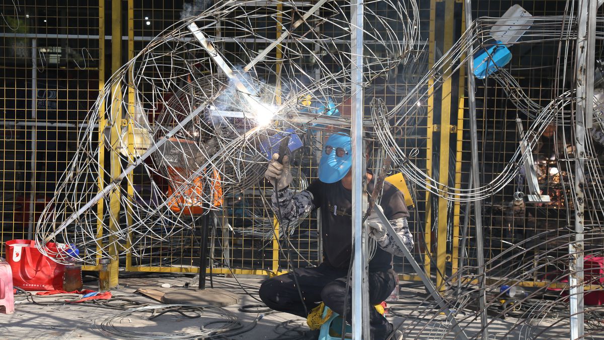 Welder wearing a face shield and gloves joining the wire frame of a large lantern