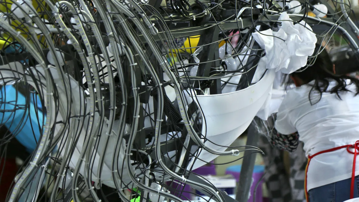 Hands covering a lantern frame with fabric and LED strip at a factory workbench